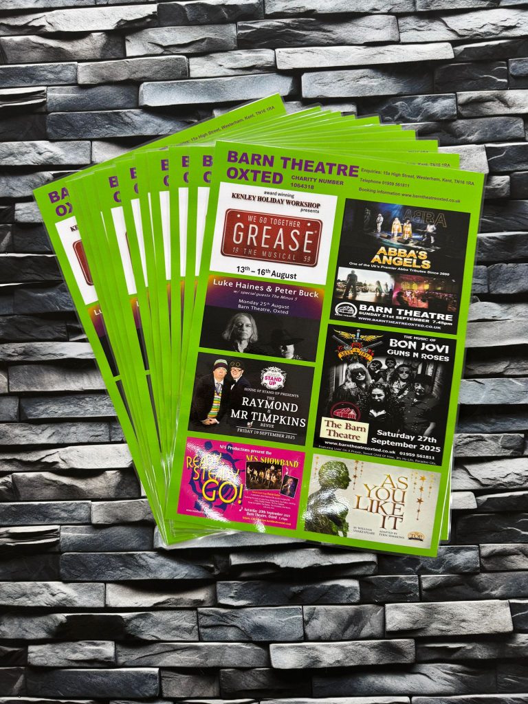 Stack of green-bordered Barn Theatre Oxted event leaflets placed on a stone background, showing upcoming theatre shows and performances.