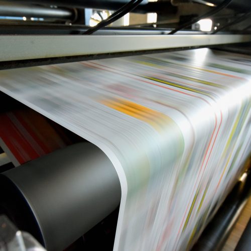 Close-up of a high-speed printing press producing colourful sheets of paper in motion.
