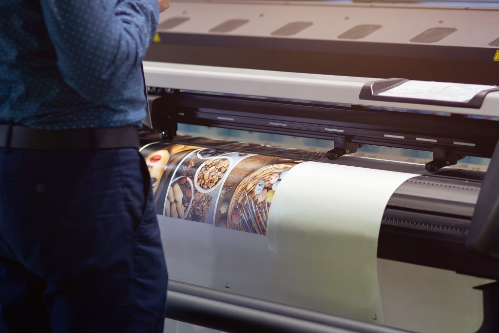 Print technician checking a large format banner coming off a wide format printer at Expresscopy